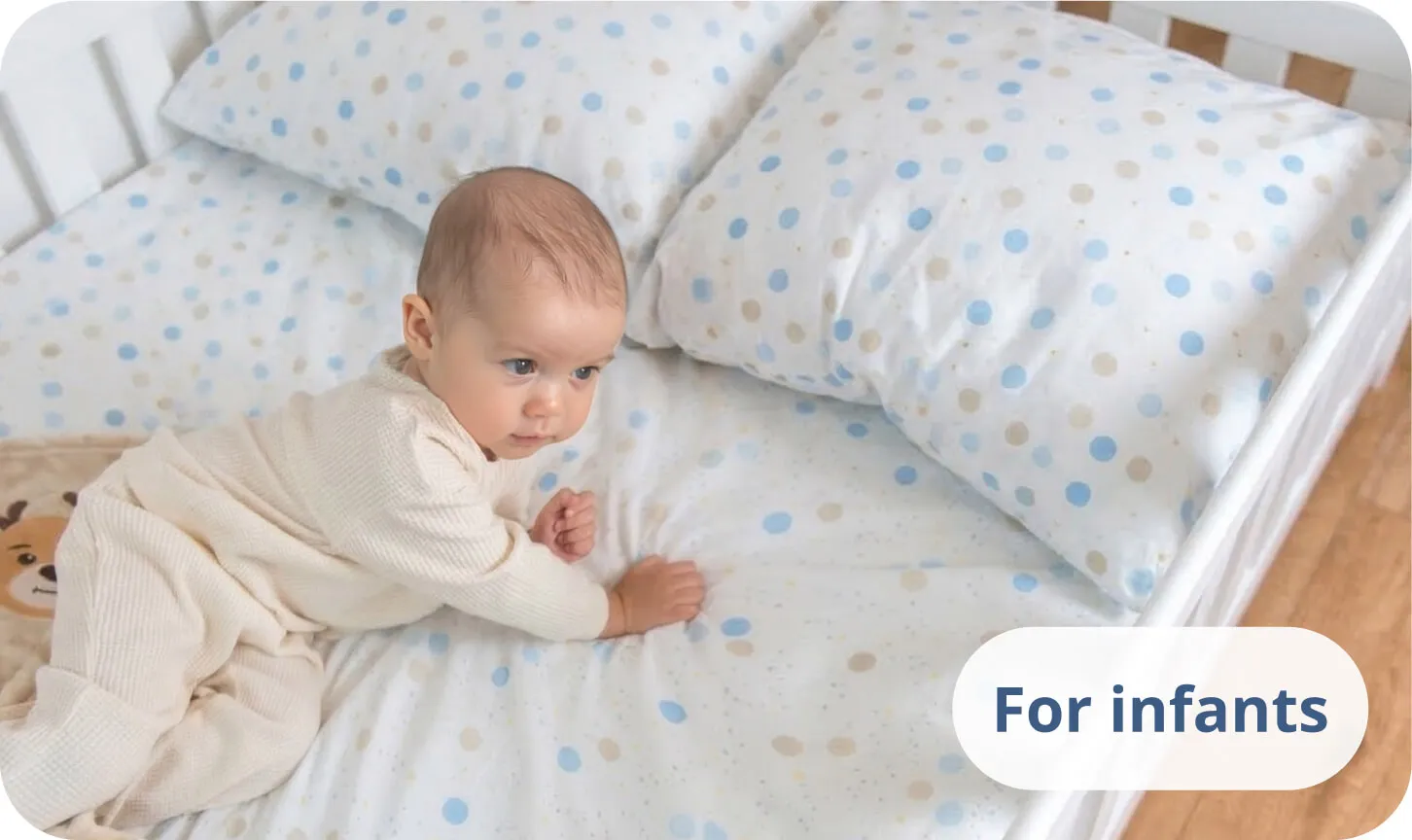 Baby lying on its stomach on a white bed with blue polka dot bedding.